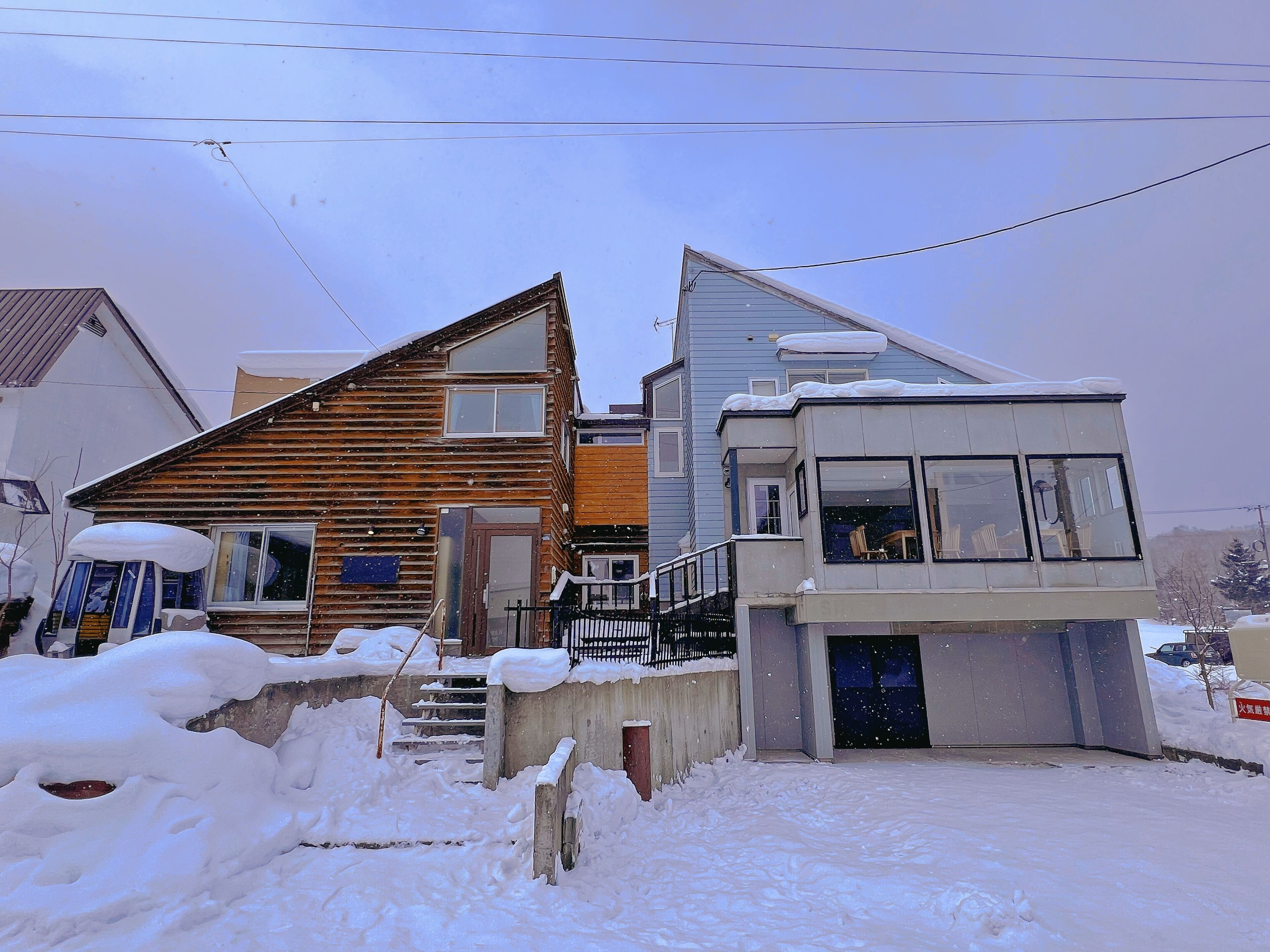 A two-story house with a wooden exterior and a modern extension with large windows. Snow covers the ground and steps.