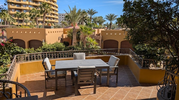 Relax on the patio surrounded by lush palm trees and enjoy a meal at the wooden table with comfortable seating.