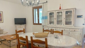 Un coin repas comprenant une table ronde, des chaises, un lustre, un téléviseur et un meuble avec des portes en verre.