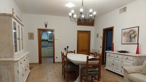 Un coin repas avec une table et des chaises en bois, un buffet blanc, un lustre et un tableau accroché au mur.