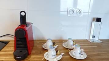 A kitchen with a red coffee machine, four white cups with saucers, and a bottle of water on the counter.