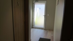 A hallway with a wooden door, a glass door with a frosted pattern, and a doormat. - Seclin Appartements (Seclin)