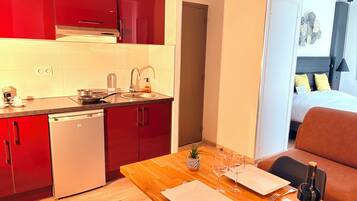 A compact kitchen with red cabinets, a dishwasher, and a dining area with a wooden table set for two.