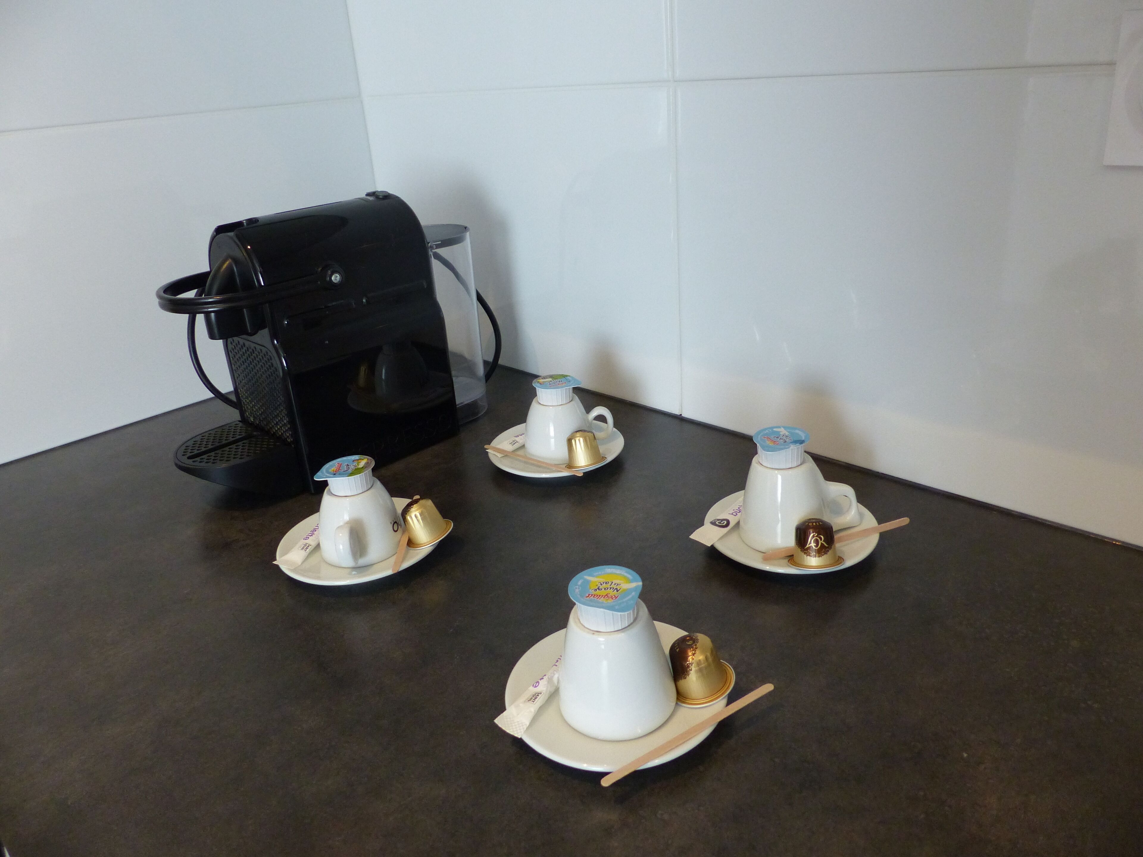Un coin cuisine avec une machine à café et quatre théières sur un plan de travail.