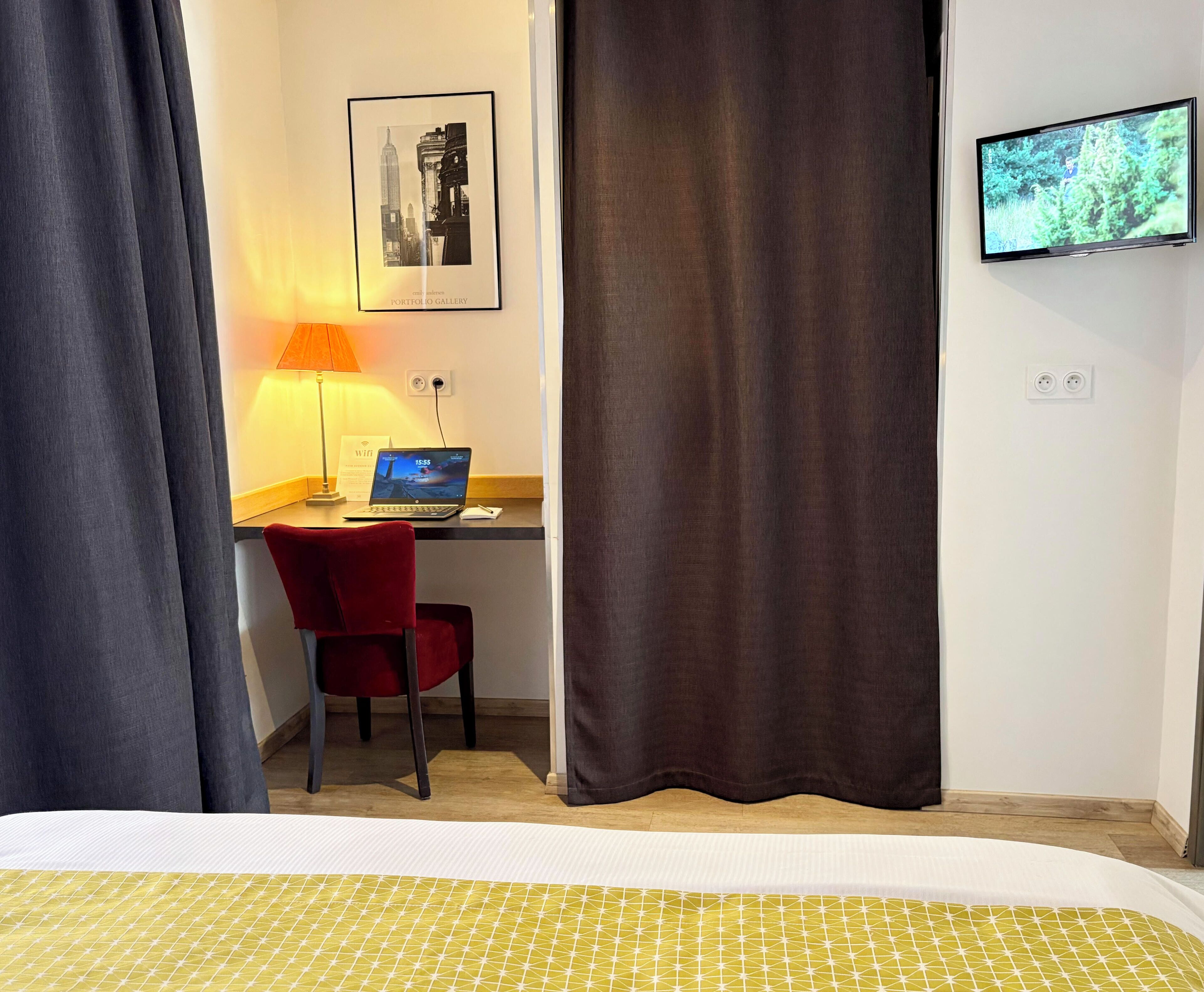 Een hotelkamer met een bed, een bureau met een laptop, een stoel, een televisie en een lijst aan de muur.