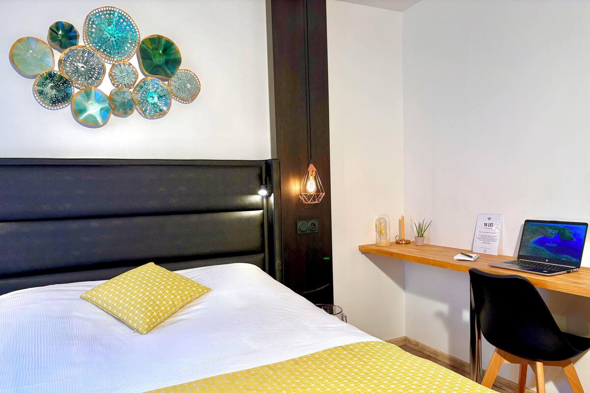 A hotel room with a bed, a desk with a laptop, and a wall decoration.