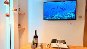 A dining area with a wooden table, a bottle of wine, a glass, and a television displaying an underwater scene. - Seclin Appartements (Seclin)