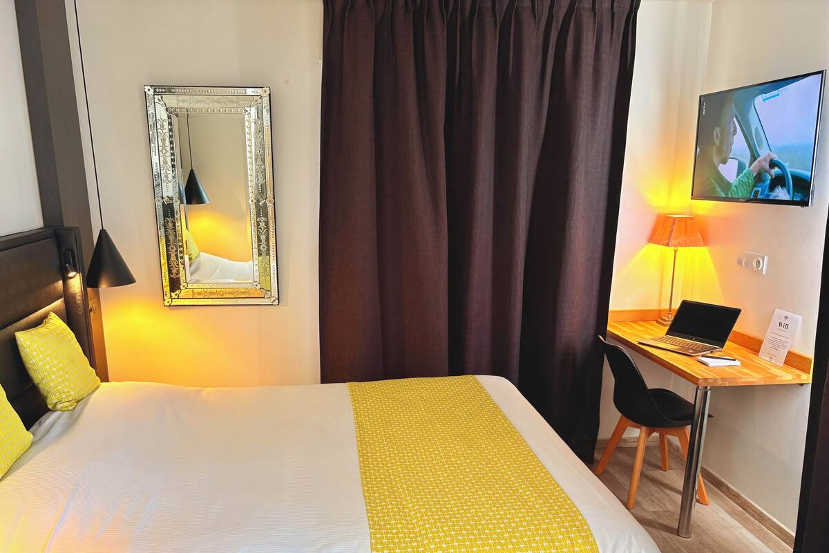 A hotel room with a large bed, a desk with a laptop, a TV, and a mirror.
