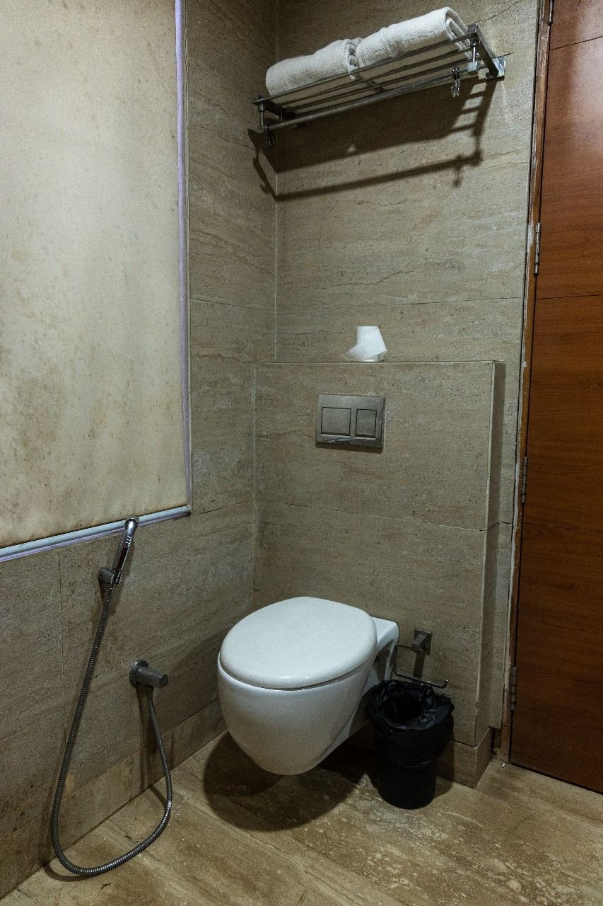 A small bathroom with a toilet, a towel rack, a trash bin, and a shower hose.