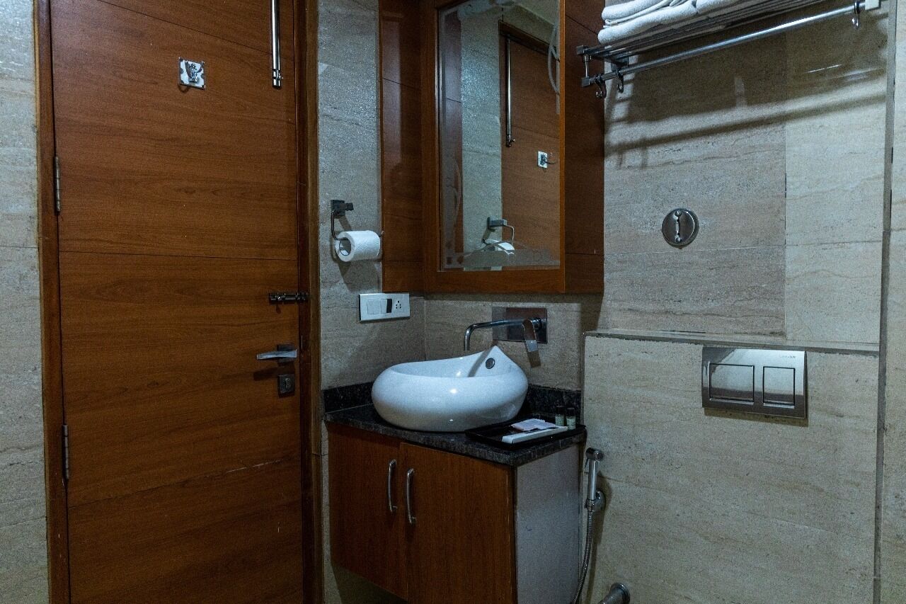 A bathroom with a wooden vanity, a white sink, a mirror, and a shower area.