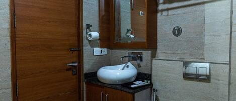A bathroom with a wooden vanity, a white sink, a mirror, and a shower area.