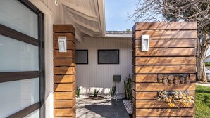 A modern building entrance with a wooden facade, a concrete pathway, and a small garden area with plants. - Luxury 3BR Oasis: Pool & Style (Costa Mesa)