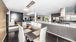 A modern kitchen with a central island, dark flooring, and white chairs. - Luxury 3BR Oasis: Pool & Style (Costa Mesa)