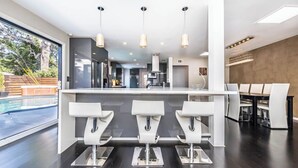A modern kitchen with a central island, three white bar stools, and pendant lighting. - Luxury 3BR Oasis: Pool & Style (Costa Mesa)