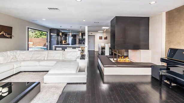 A modern living room with a sectional sofa, a fireplace, a piano, and a dining area in the background. - Luxury 3BR Oasis: Pool & Style (Costa Mesa)