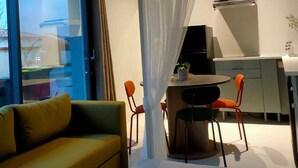 Een moderne woonkamer met een groene bank, een eettafel met twee stoelen, en een keuken met een fornuis en kasten.