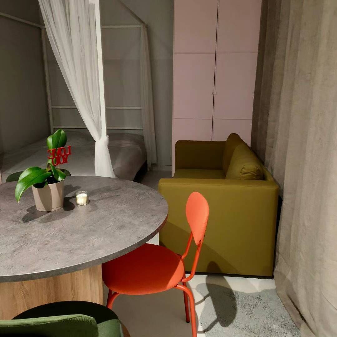 Une petite pièce moderne avec une table ronde, une seule chaise orange, un canapé vert et une plante en pot.