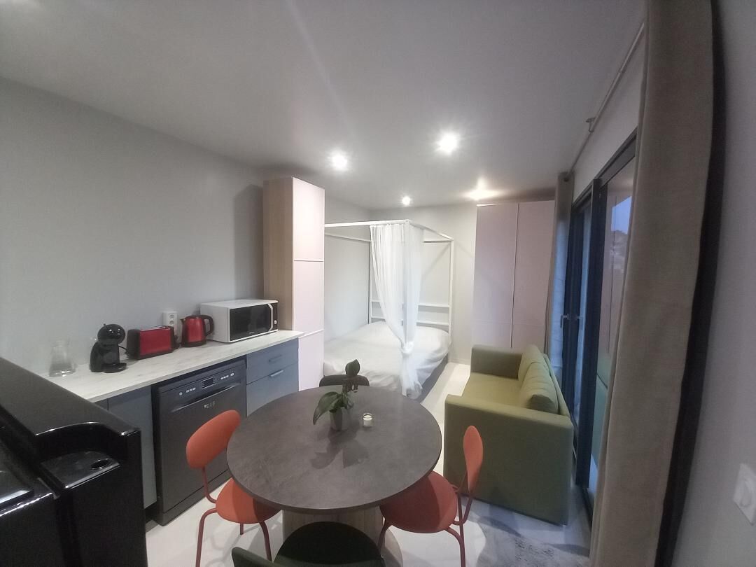 Una habitación de hotel compacta con kitchenette, zona de comedor, cama con dosel y sofá.