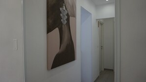 A hallway with a large abstract painting on the wall, a door at the end, and a light switch on the wall. - La Scala del Moro Rooms- Dolce Risveglio (Lampedusa)