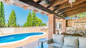 Un espace aménagé au bord de la piscine, avec une piscine aux formes arrondies, des meubles en osier et un mur en pierre.