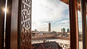 A view from a balcony with a patterned wooden partition, a metal railing, and a distant view of a tower and domed structures. - terrace suzangaron  (Bukhara)