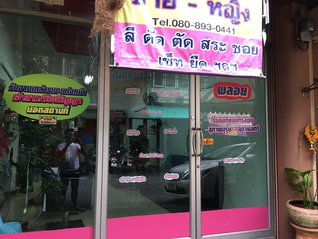 A storefront with a pink and yellow signboard, a glass door, and a reflection of a person and a car.
