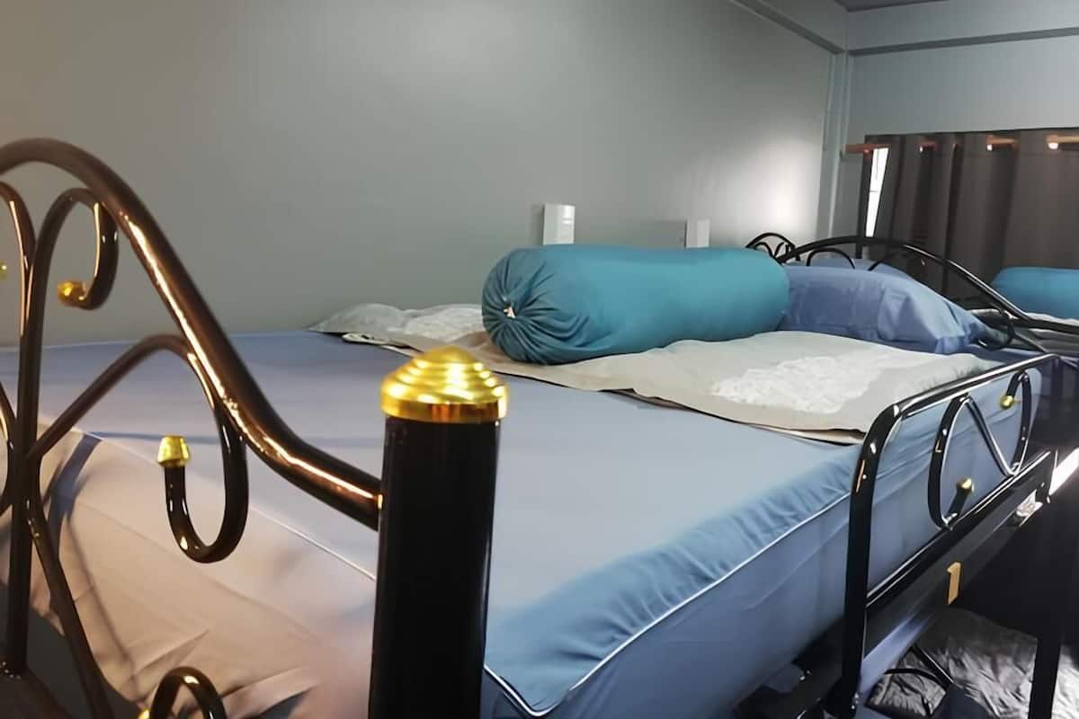 A single bed with a blue mattress and a white pillow, a bedside table with a lamp, and a wall-mounted shelf.
