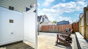 Patio trasero con terraza de madera, un parque infantil y una puerta blanca.