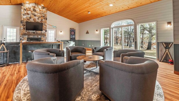 A cozy living room with a stone fireplace, comfortable seating, and large windows offering a view of the outdoors.