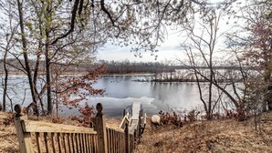 A wooden boardwalk leading to a lake with a view of trees and a distant shoreline.