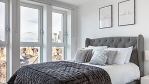 A modern bedroom with a large bed, two windows, and city views.