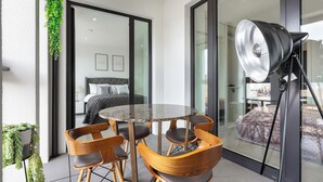 A modern room with a round table and six wooden chairs, a large window with a view, and a floor lamp.