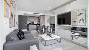 A modern living room with a grey sofa, a coffee table, and a dining area with grey chairs.