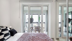 A modern hotel room with a large bed, a balcony with a dining area, and a view of the city.