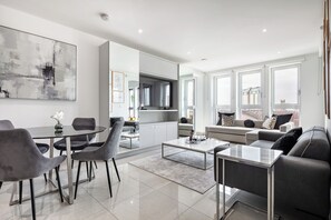 A modern living room with a dining area, a kitchen, and a large window with a city view.