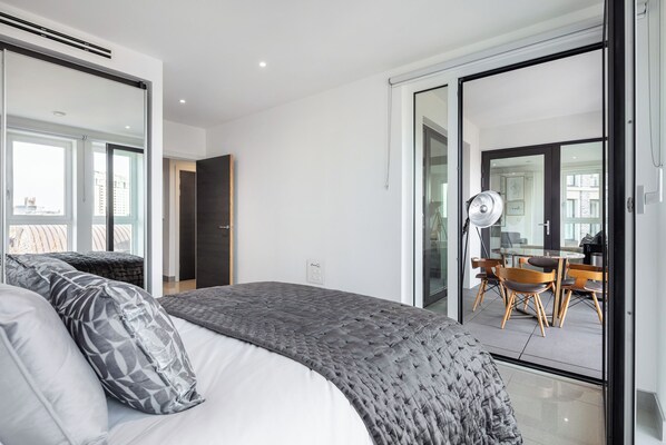 A modern bedroom with a large bed, a desk, and a chair in the adjacent room.