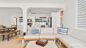 A modern living room with a sofa, a coffee table with a chess set, and a dining area with a wooden table and benches. - Casa Bella with private swimming pool (Aguada)