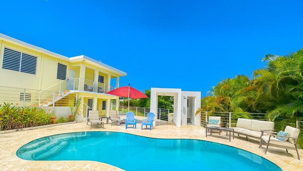 A pool area with a curved pool, lounge chairs, and a red umbrella. - Casa Bella with private swimming pool (Aguada)