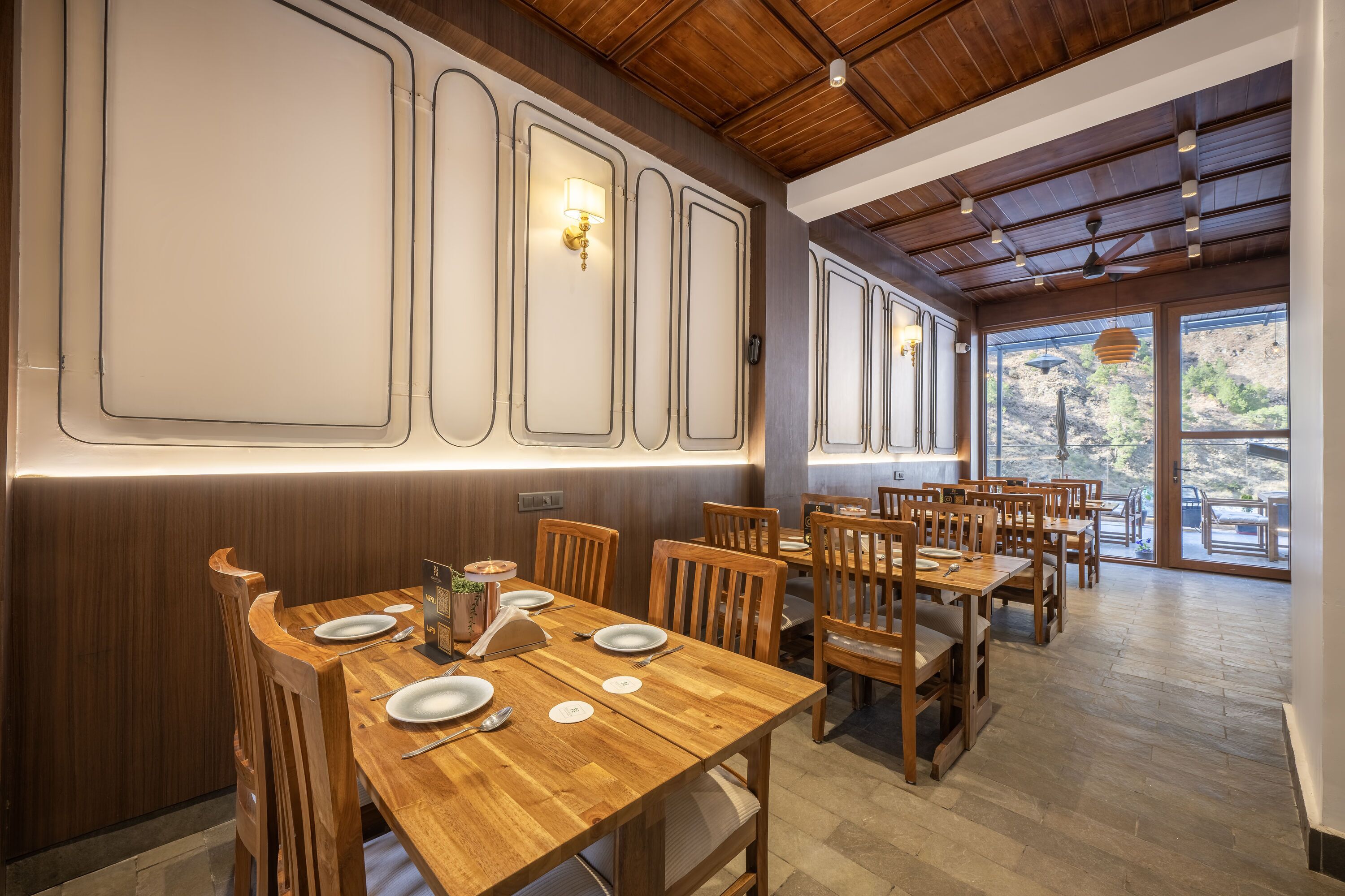 A restaurant with wooden tables and chairs, a high ceiling with exposed beams, and a view of the outdoors through large windows.