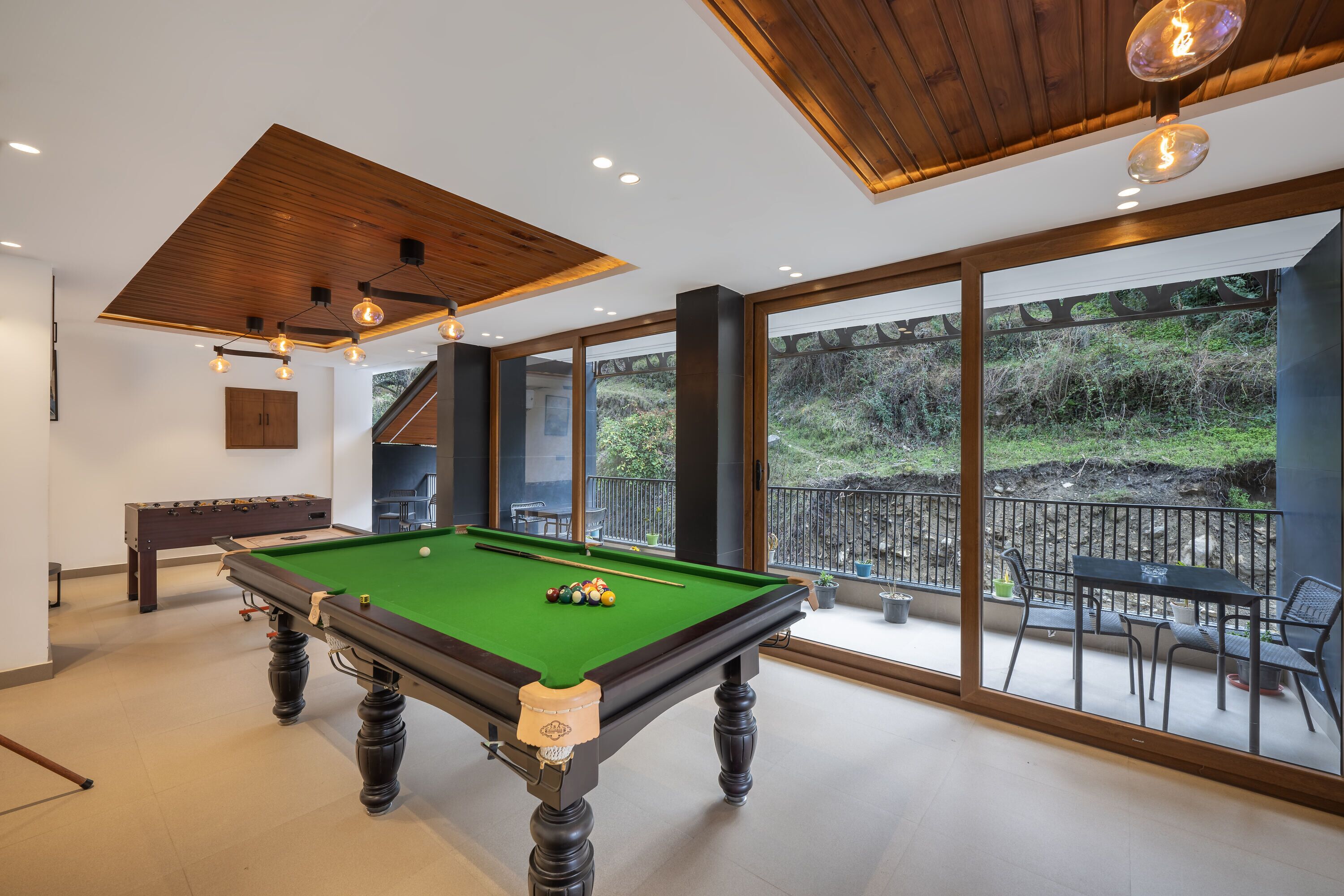 Une table de billard avec des billes, une table de baby-foot et un escalier menant à un balcon avec des sièges d’extérieur.