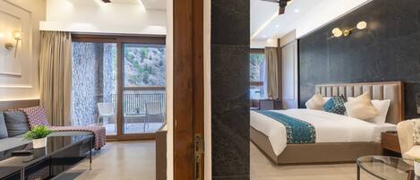 A modern hotel room with a bed, a sofa, a coffee table, and a balcony with a view of the mountains.