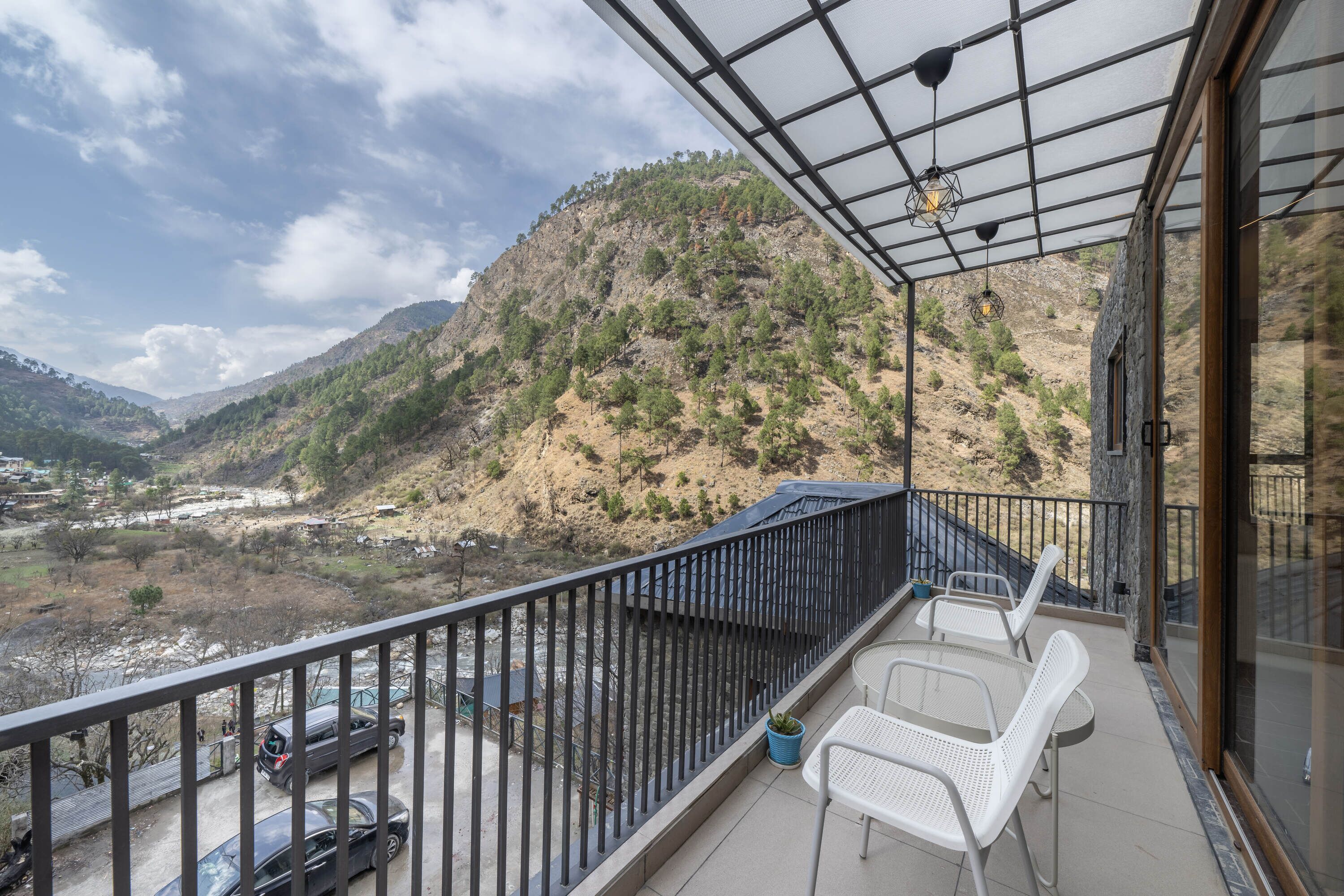 Un balcon donnant sur un paysage montagneux, une table avec des chaises et une voiture garée à l’extérieur.