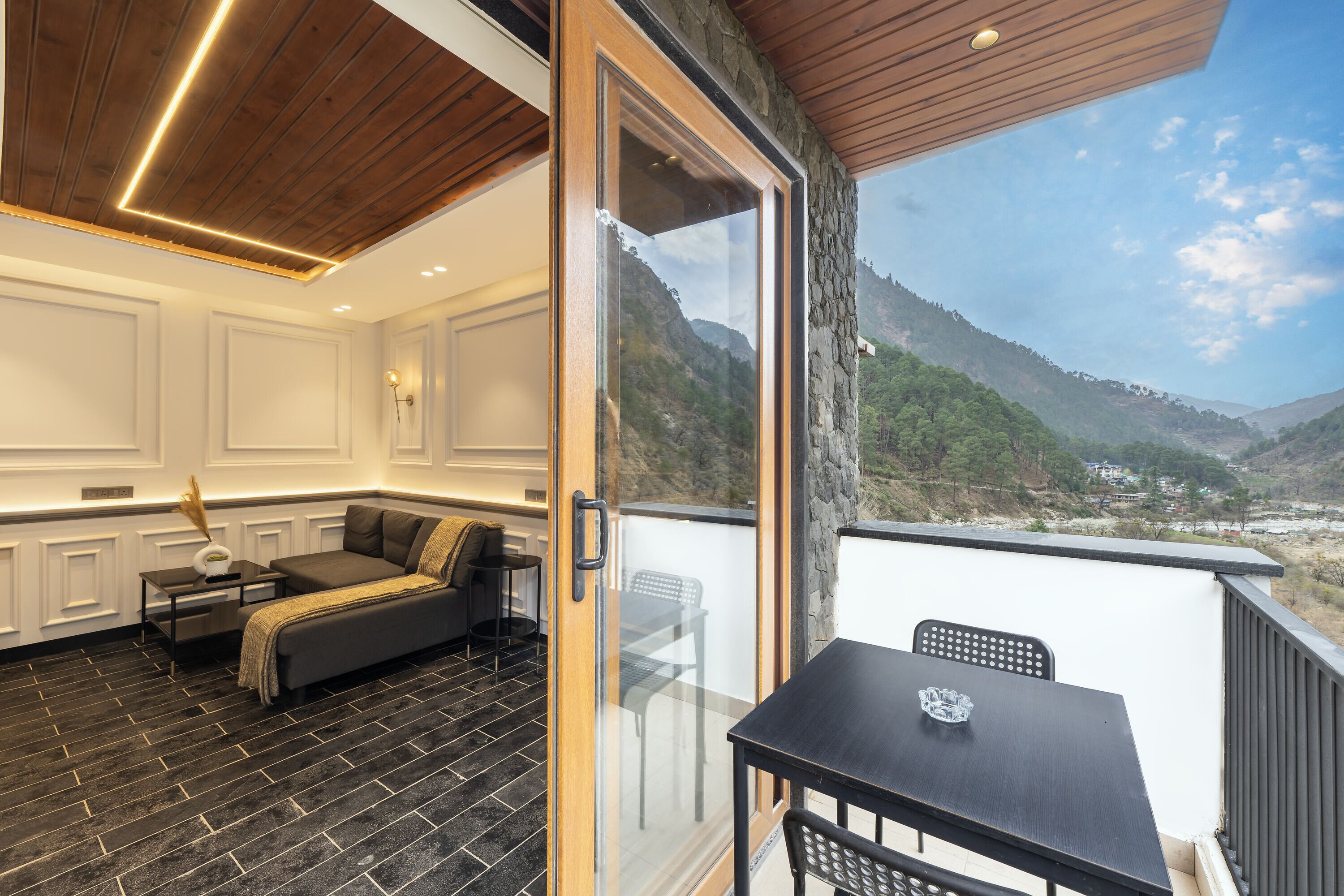 A modern room with a dark tiled floor, a sofa, a table, and a balcony with a mountain view.