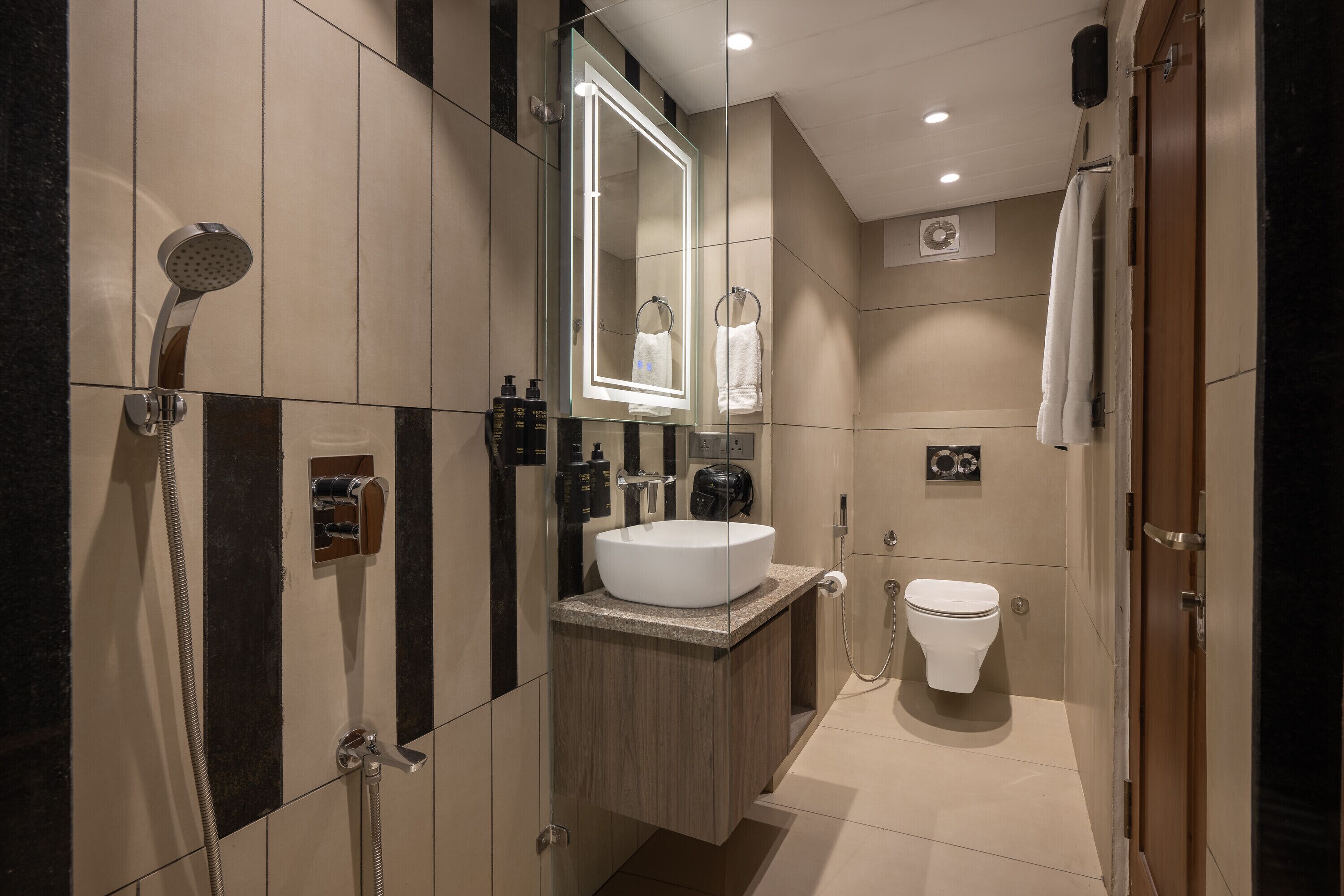 Un baño moderno con un espejo grande, un lavabo blanco, una ducha y un inodoro.