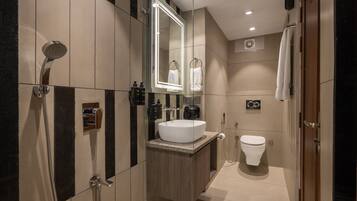 A modern bathroom with a large mirror, a white sink, a shower, and a toilet.