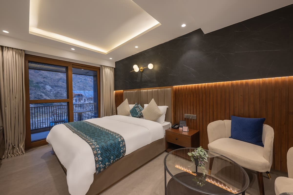 A modern hotel room with a large bed, a glass coffee table, a seating area, and a view of the outdoors.