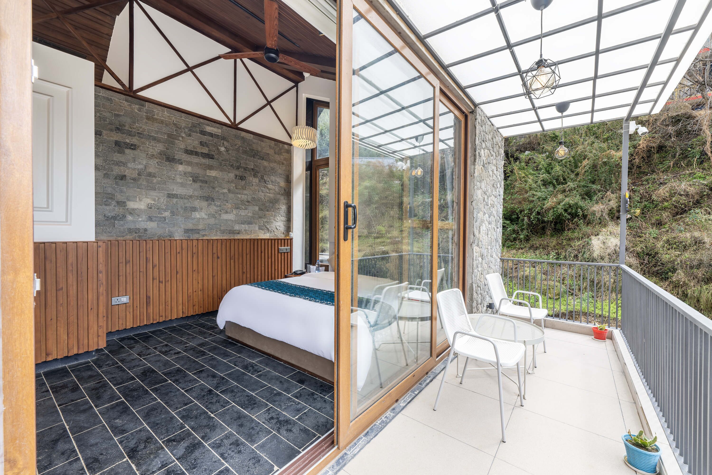 A bedroom with a large bed, wooden paneling, and a glass door leading to a balcony with chairs and a table.