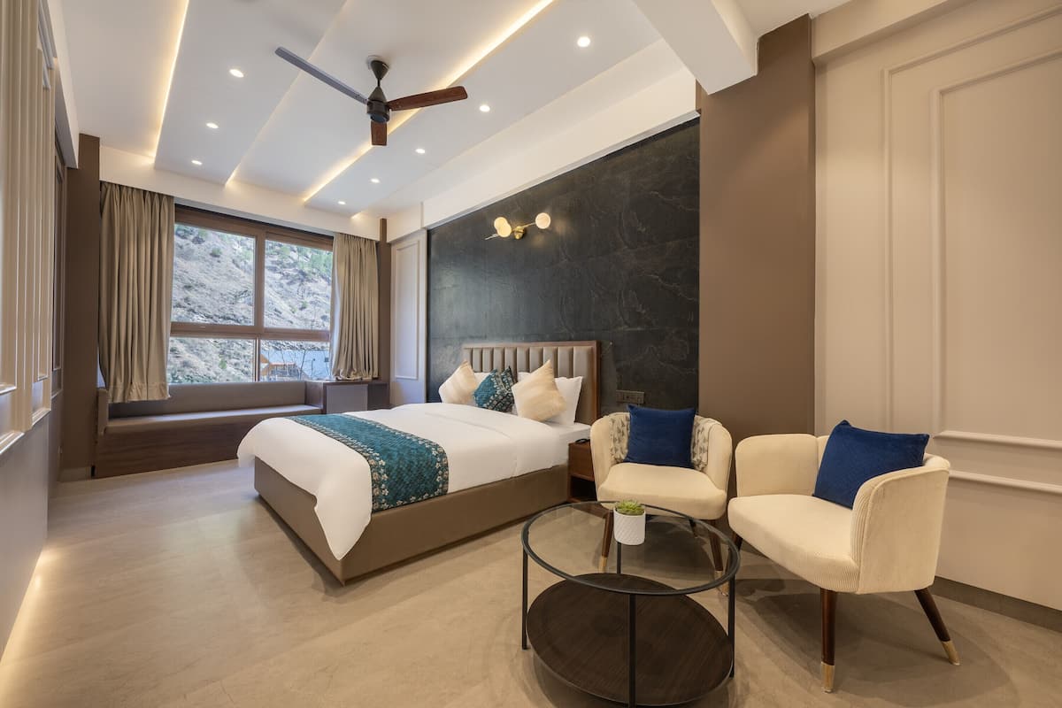 A modern hotel room with a large bed, a sofa, a glass coffee table, and a ceiling fan.