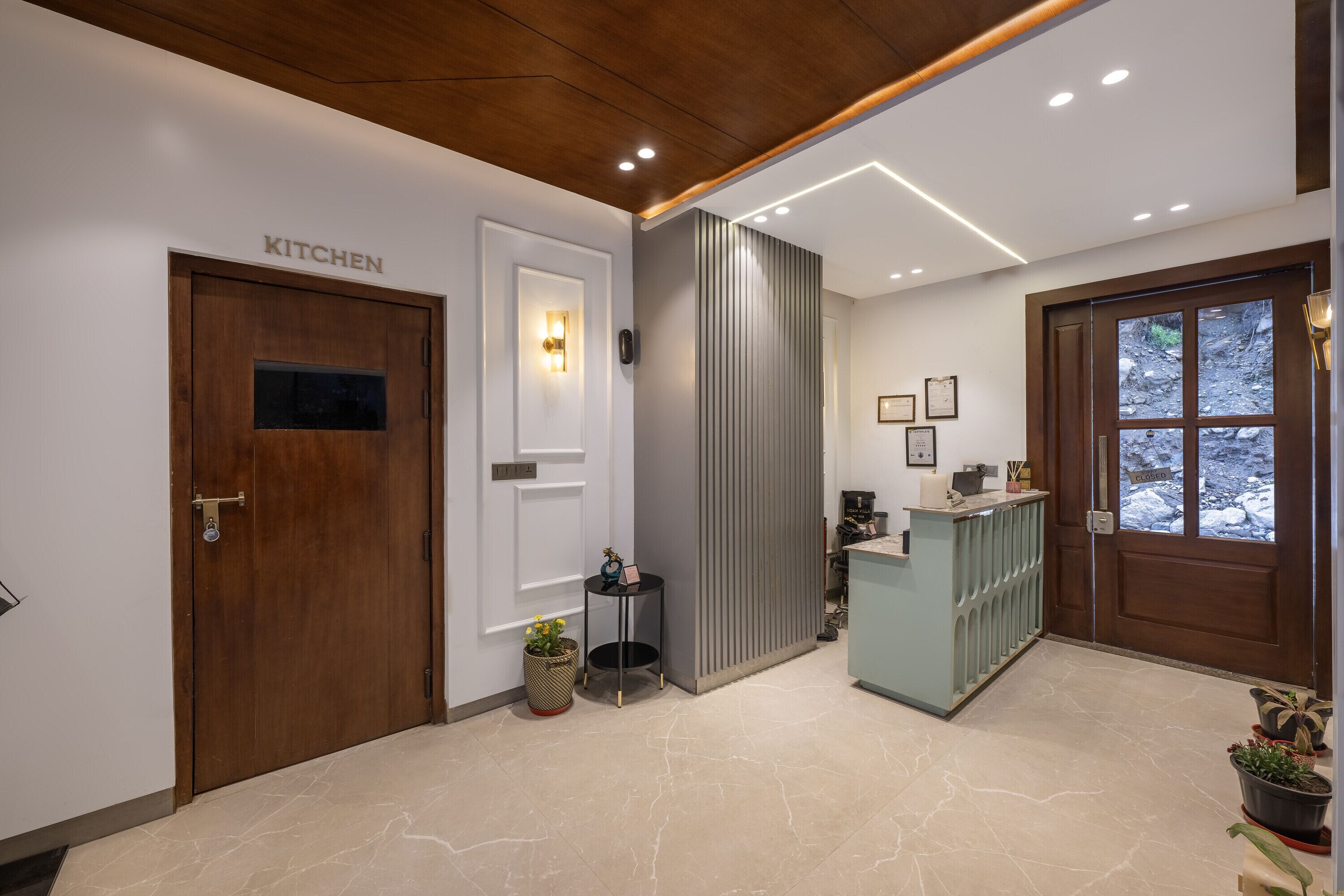Un área de cocina moderna con una puerta de madera que dice 'KITCHEN', una pequeña mesa con una planta y una lámpara sobre la puerta.