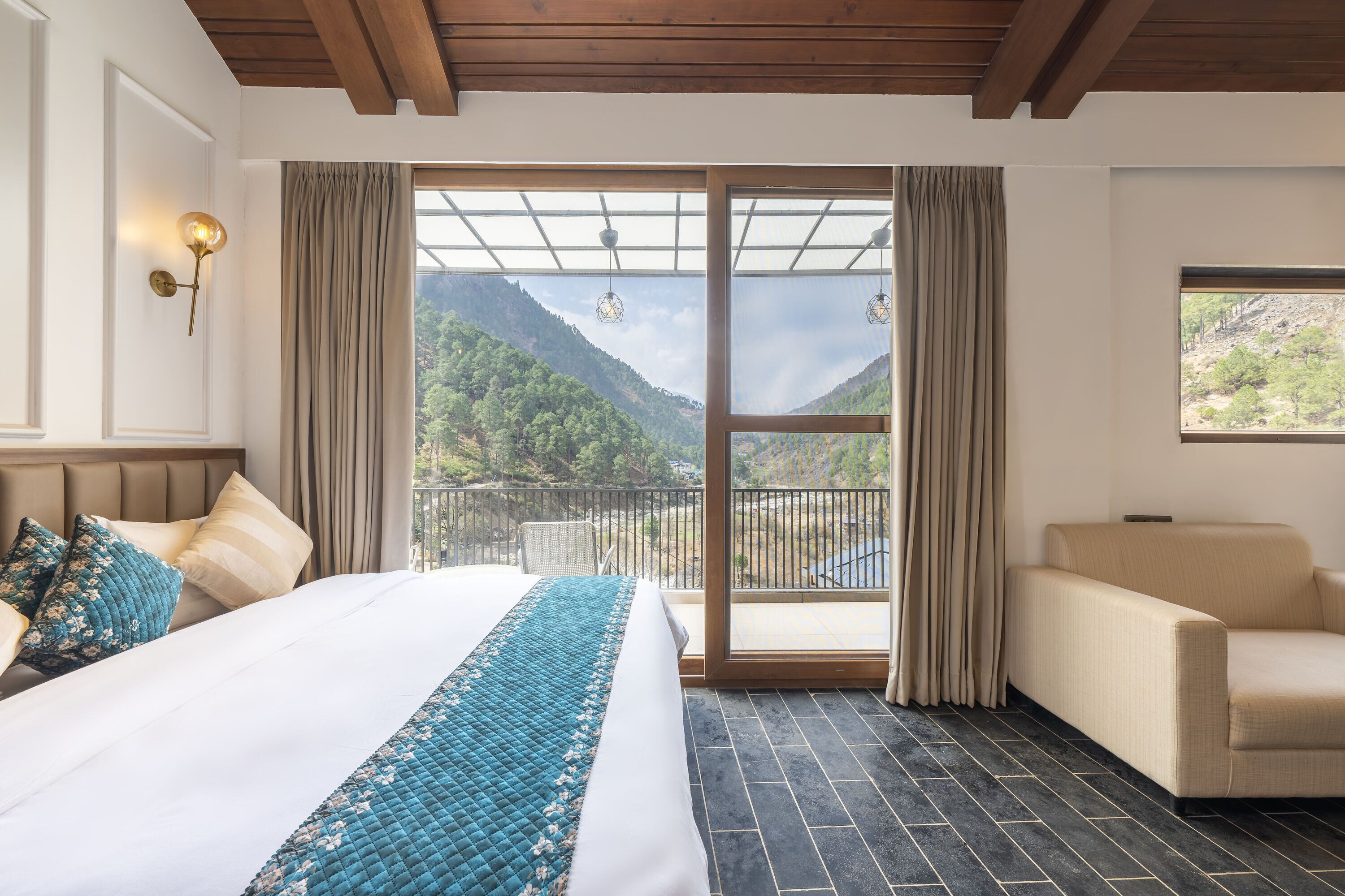 Un dormitorio con una cama grande, un sofá, vistas a montañas a través de un ventanal y un balcón.